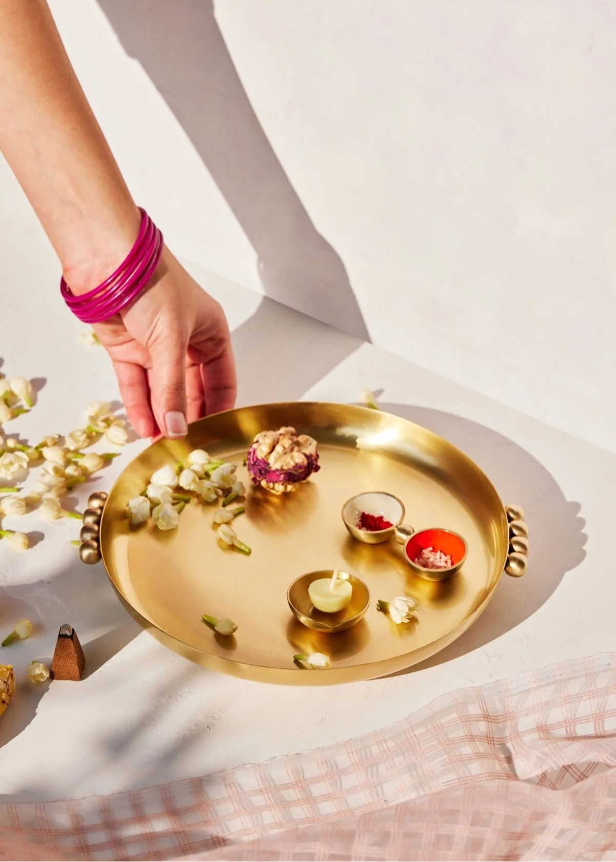 Gold tray with offerings on a white surface, hand holding a pink bracelet.
